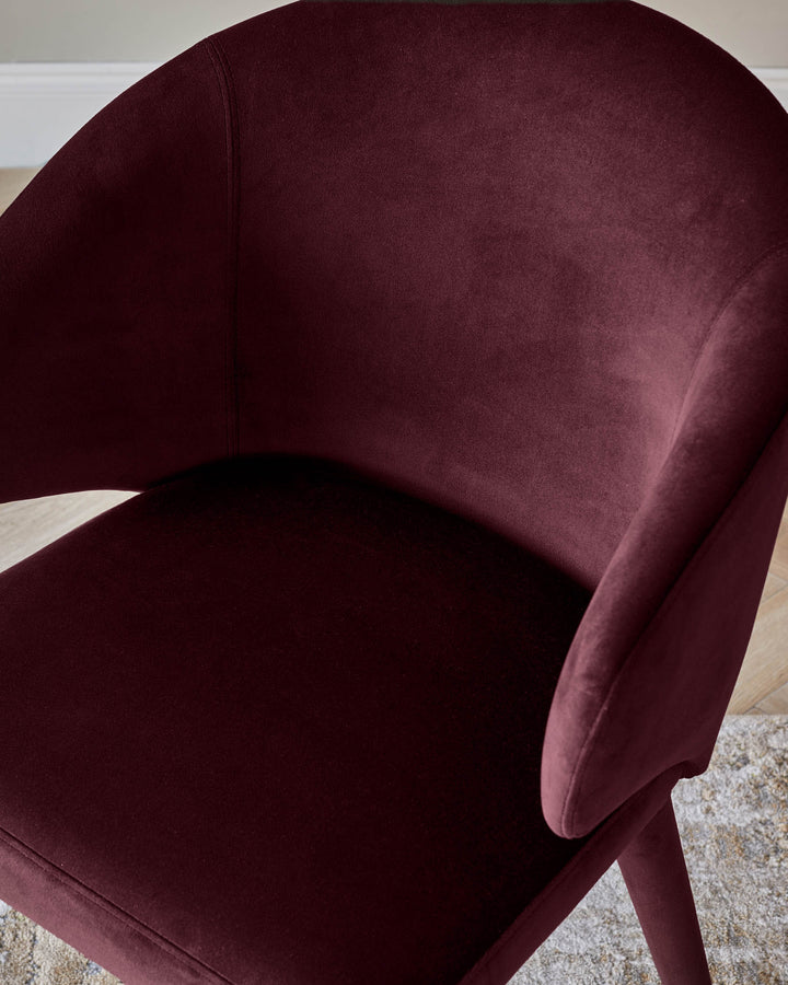 Ethan dining chair in plum velvet, showing curved backrest and seat from a side angle on a light area rug.