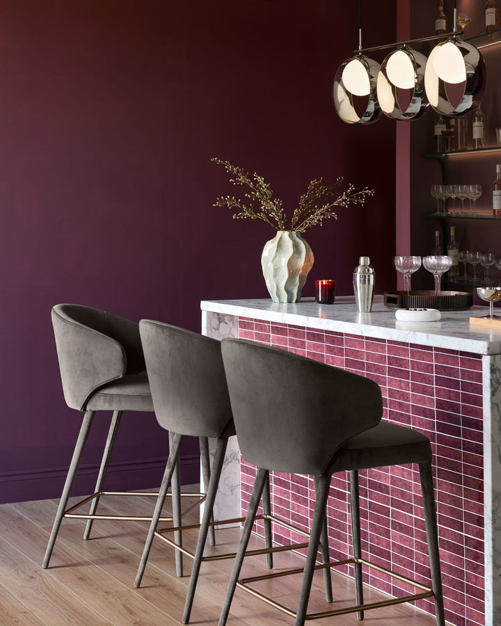 Ethan bar stool in dark chocolate velvet, shown as a pair at a burgundy tiled bar with marble countertop in a modern lounge setting.