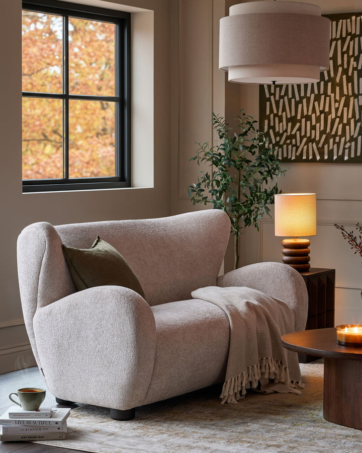 Cream fabric 2-seater sofa with curved arms and rounded back, displayed in a cozy living room setting.