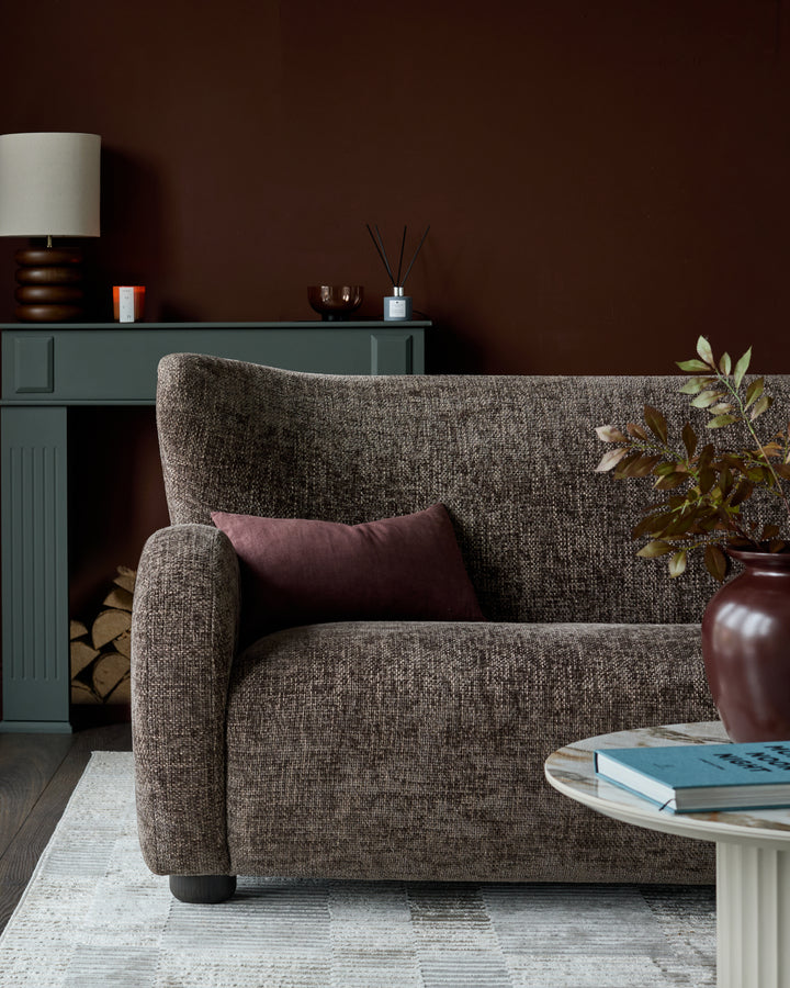Evelyn 2-seater sofa in mocha fabric, angled view showing textured upholstery, rolled arms, and burgundy accent pillow.