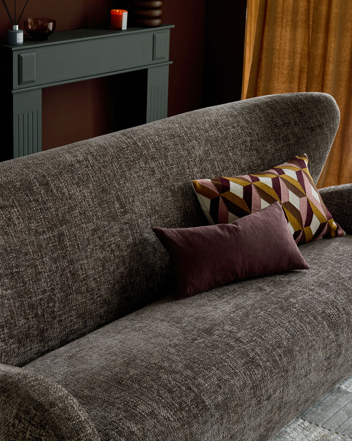 Evelyn 3-seater sofa in mocha fabric, featuring curved arms and decorative pillows in burgundy and geometric patterns.