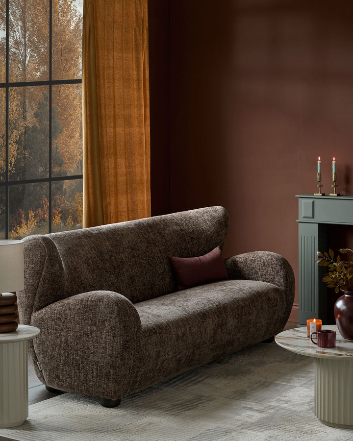 Evelyn 3-seater sofa in mocha fabric with curved arms and back, displayed in a warm, styled living room setting.