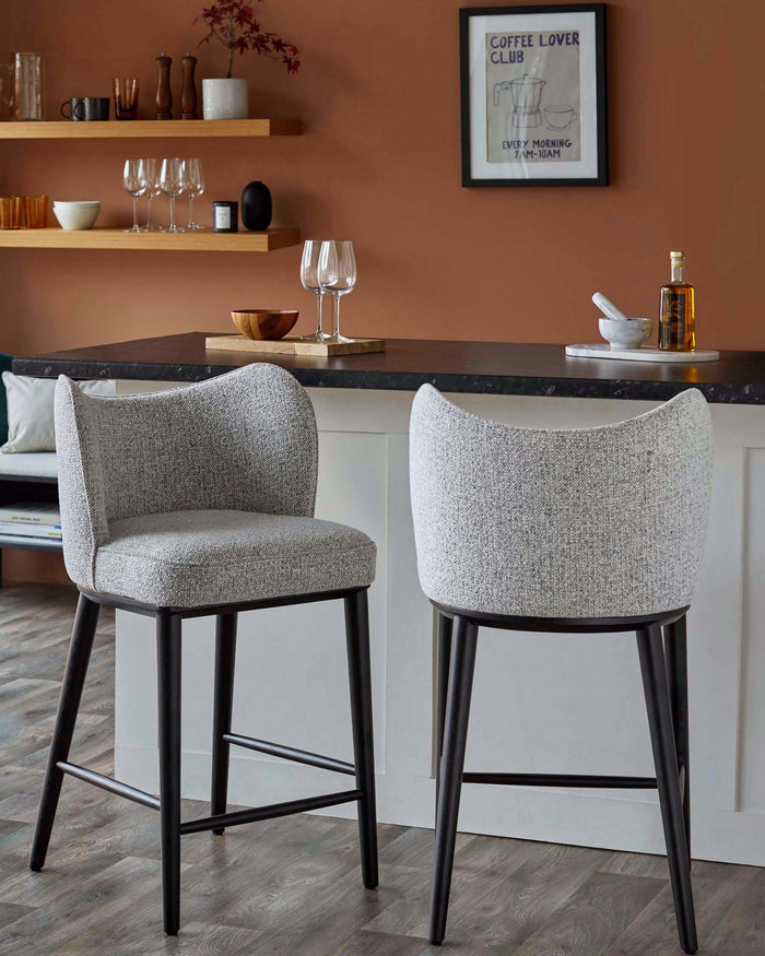Two grey upholstered bar stools with dark wooden legs sit in front of a kitchen island, adding a touch of modern elegance.