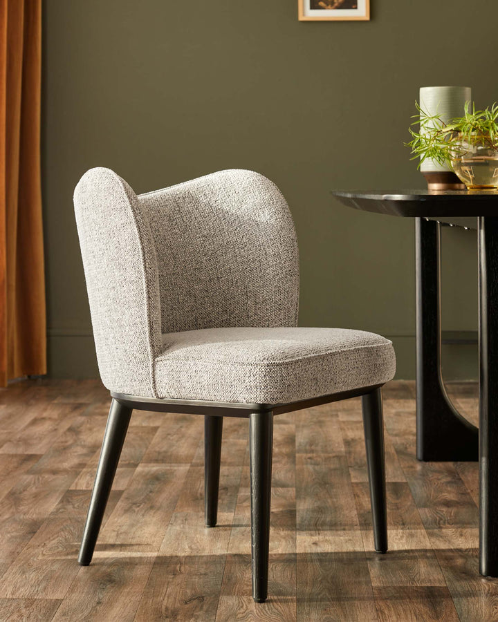 An upholstered dining chair with curved back sits beside a dark wood table on a wooden floor.