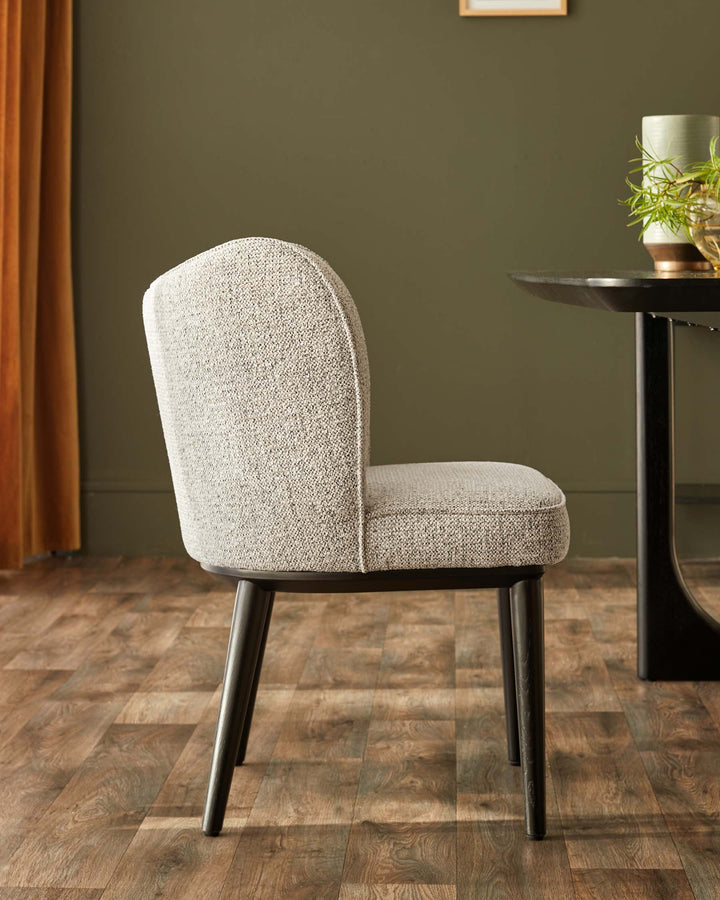 Stylish grey upholstered dining chair with dark wooden legs, next to a modern black table on a wooden floor.