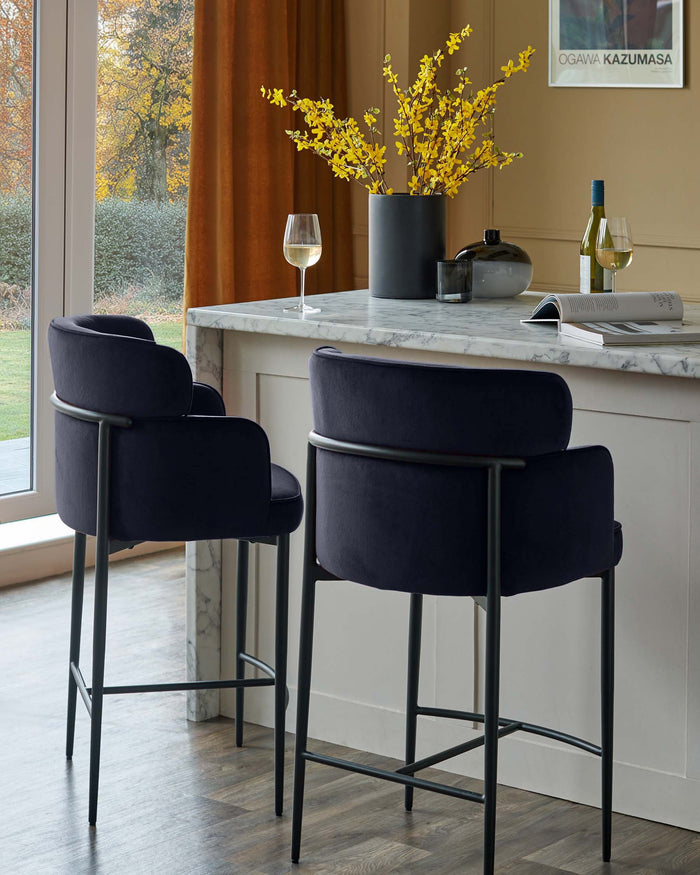 Two luxurious navy velvet bar stools with sleek black frames sit at a marble-topped kitchen island, exuding modern elegance.