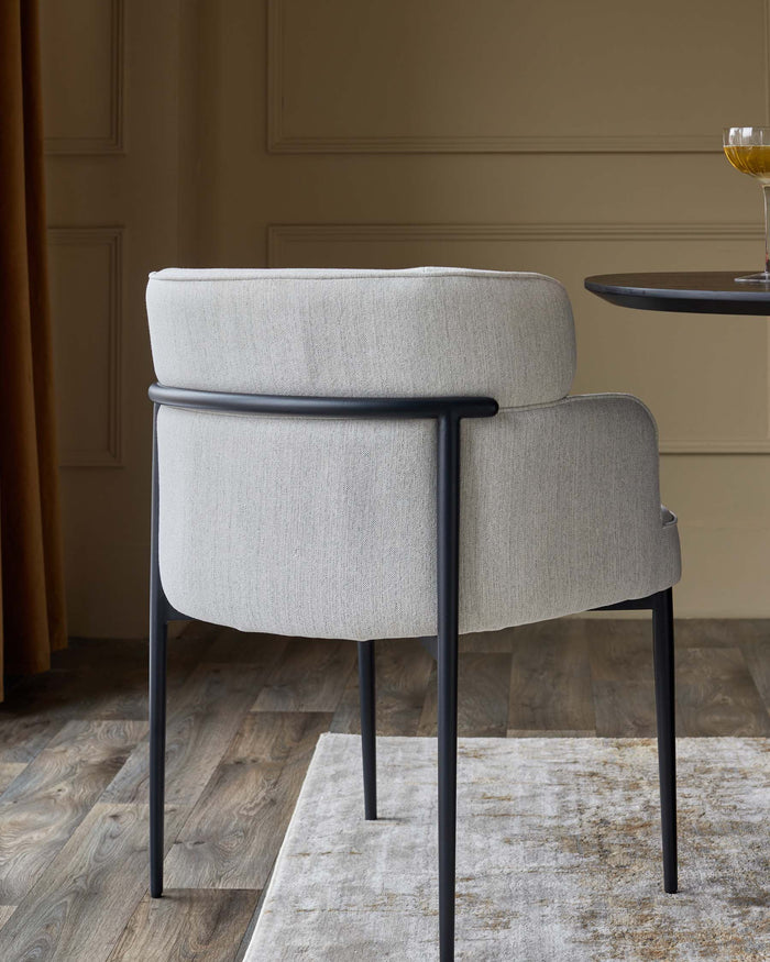 Upholstered chair with sleek metal frame sitting atop a patterned rug, next to a dark wood table.