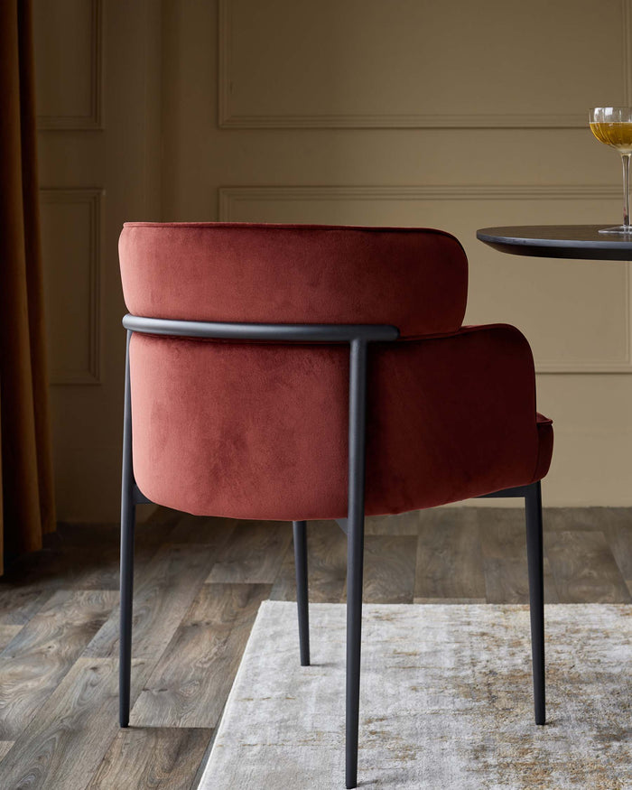 A red velvet chair with black metal frame, positioned on a rug. A table and wine glass are nearby.