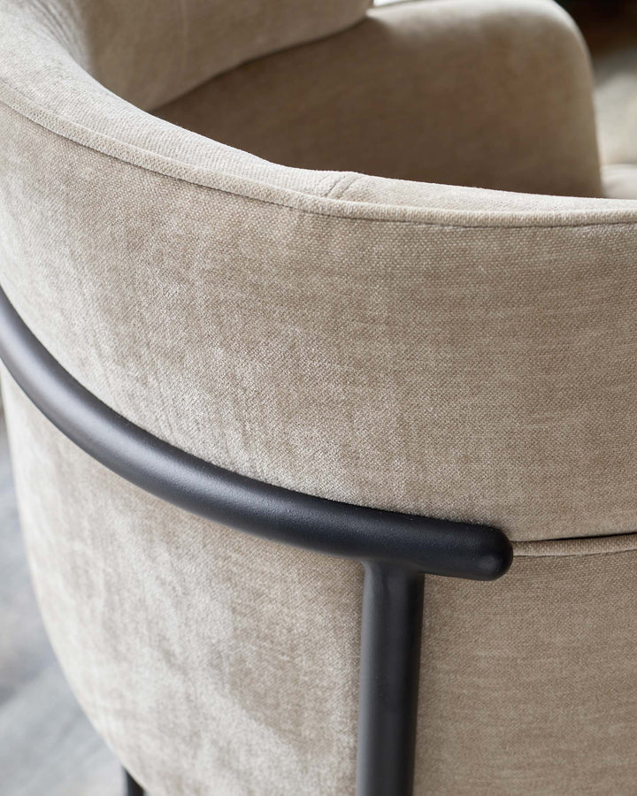 Close-up of a beige upholstered armchair with a curved back and black metal frame, showcasing its texture and design.