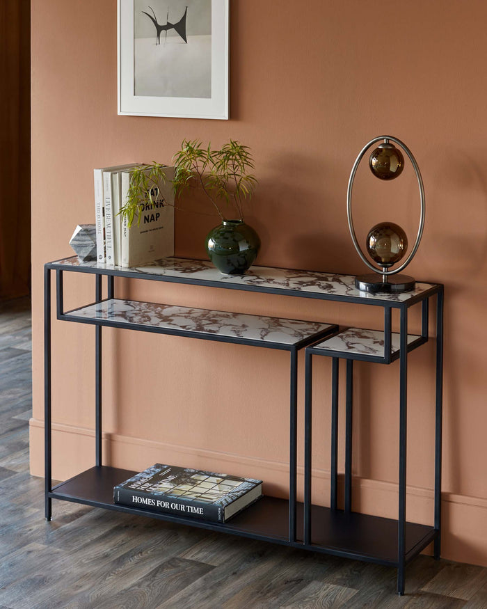 Black metal console table with marble-effect tops, featuring books, a vase, and a modern lamp.