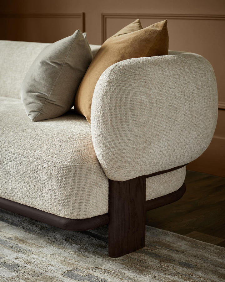 Beige sofa with rounded arm and bolster cushions in brown and beige, on a patterned rug.