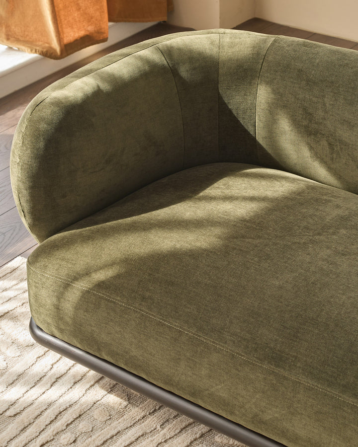 Olive green curved armchair with rounded backrest and seat, dark wood base, displayed on striped neutral rug.