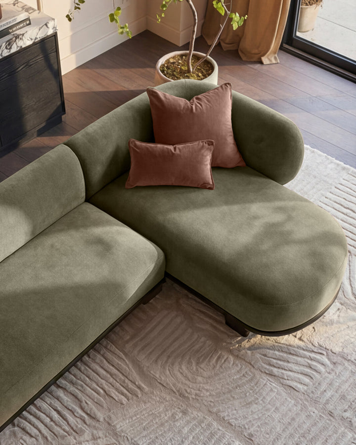 Florence right-hand facing chaise sofa in olive green with dark wood base, styled with burgundy cushions in a modern living room.