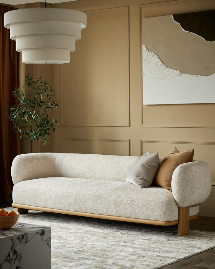 A cosy cream sofa with scatter cushions sits on a patterned rug, beneath a tiered light fitting and abstract art.