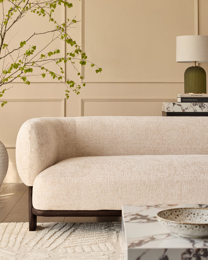 Florence 2-seater sofa in natural fabric with curved arms and dark wood legs, shown in a styled living room setting.