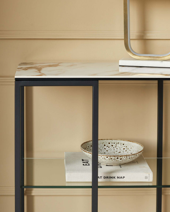 A contemporary side table with a marble top and glass shelf, displaying a stylish bowl and book.