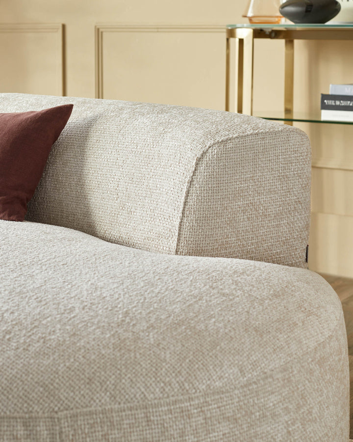 Close-up of a stylish, curved sofa with textured upholstery and a maroon pillow. A sleek gold table sits in the background.