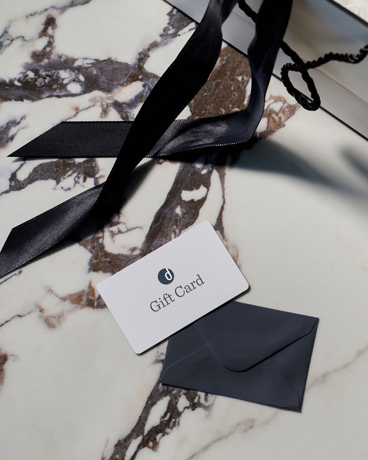 A gift card and envelope sit on a marble surface next to a partially visible shopping bag with a black ribbon handle.