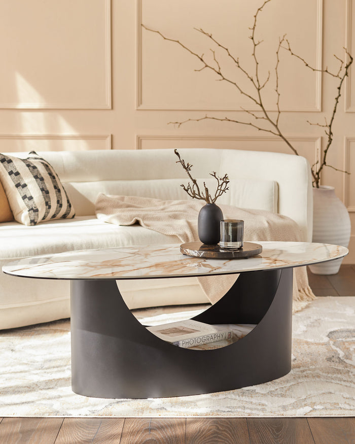 A stylish living room featuring a sofa, an oval coffee table with a marble top and black base, and a decorative vase.