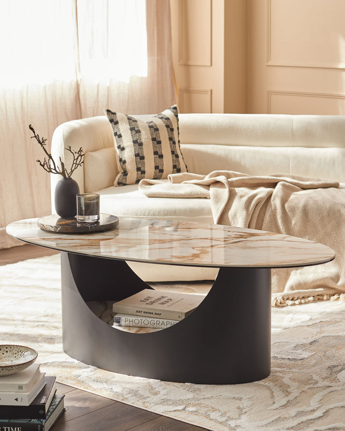 A modern living room featuring an oval marble coffee table, cream sofa with patterned cushion, and books displayed in its base.