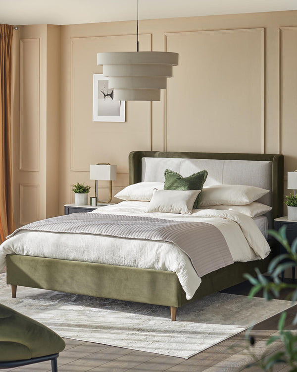A stylish bedroom suite with a green velvet bed frame, neutral bedding and a multi-tiered lampshade.