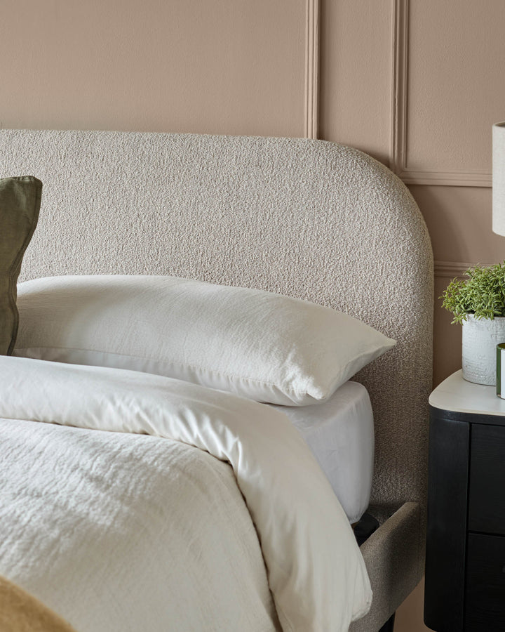 Bedroom with a neutral colour scheme, featuring a headboard with a textured fabric finish and a black bedside table.