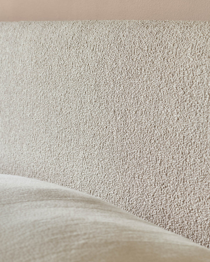 Close-up of a neutral-toned, textured headboard and a portion of the upholstered bed frame. Modern bedroom furniture.