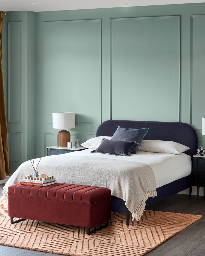 A bedroom with a bed, bedside tables, a storage ottoman, and an area rug, for a stylish and functional space.