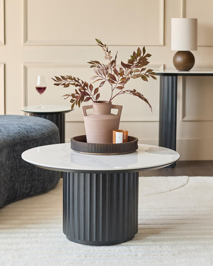 Stylish living room furniture: A round coffee table with marble top, a lamp table and a grey pouffe on a cream rug.