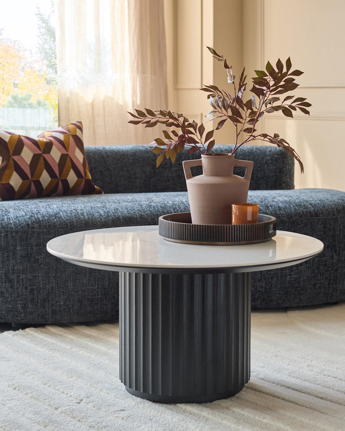 A modern living room featuring a stylish grey sofa, a patterned cushion and a round coffee table with a floral arrangement.