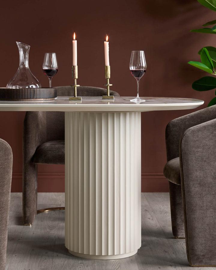 A round, cream table with a fluted base and brown velvet chairs, complete with wine glasses and candles.