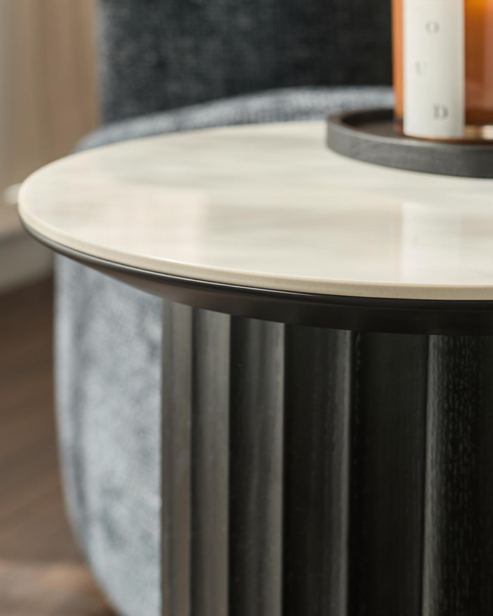 A modern side table with a marble top and a dark wood, fluted base.