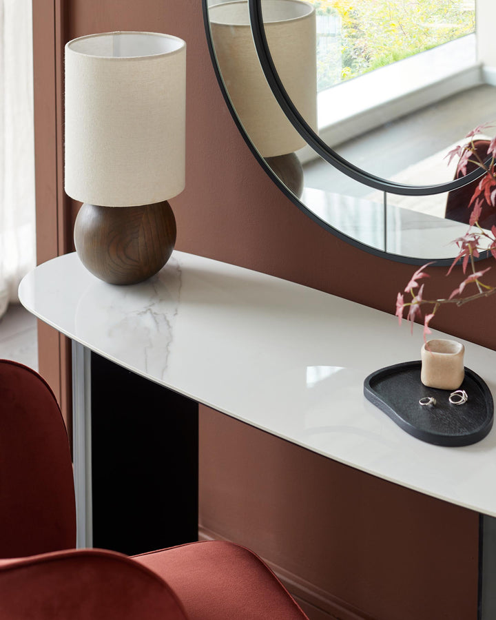 Marble-topped console table with round mirror above, complemented by a stylish lamp and accessories. Part of red chair visible.