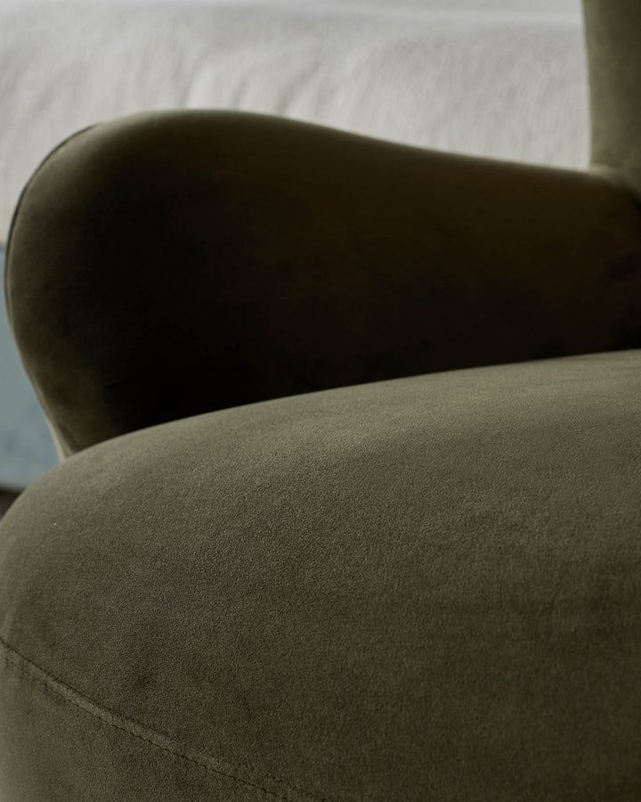 Close-up of a stylish olive green velvet armchair. The textured fabric and curved armrest suggest comfort and modern design.