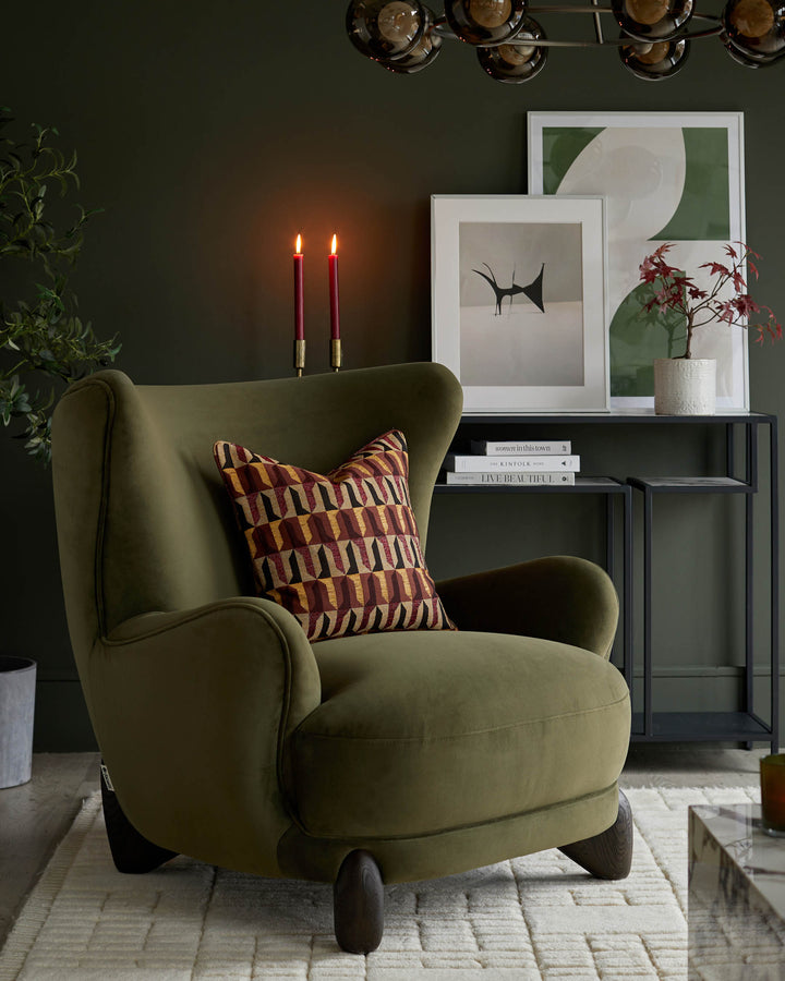 Olive green armchair with patterned cushion. A console table displays artwork, candles and a potted plant.
