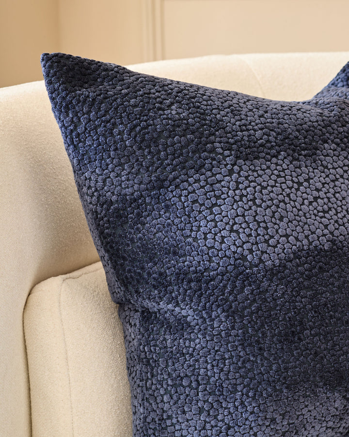 Navy textured cushion with boucle weave displayed on a cream upholstered armchair.