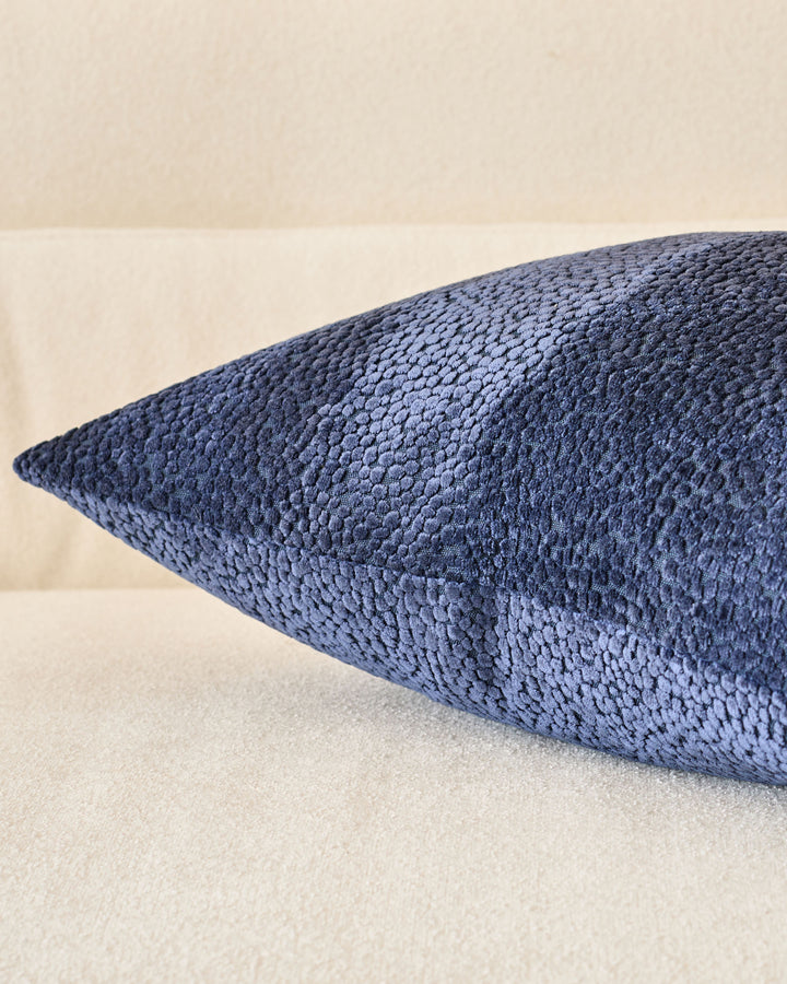 Navy blue textured cushion with pointed ends, displayed at an angle against a cream background.