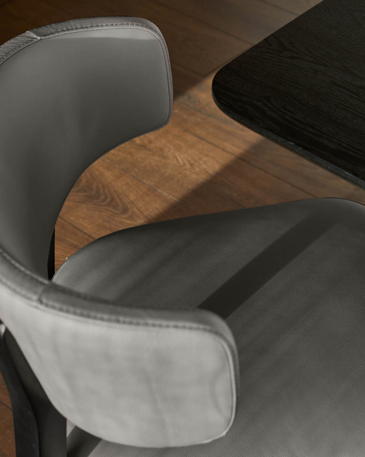 Close-up of a modern grey leather chair next to a dark wooden table on a wood floor.