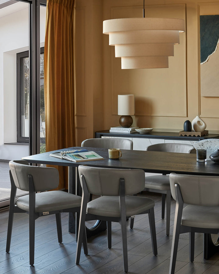 A modern dining room with a dark wood table, beige chairs, and a tiered pendant light. A sideboard adds extra storage.