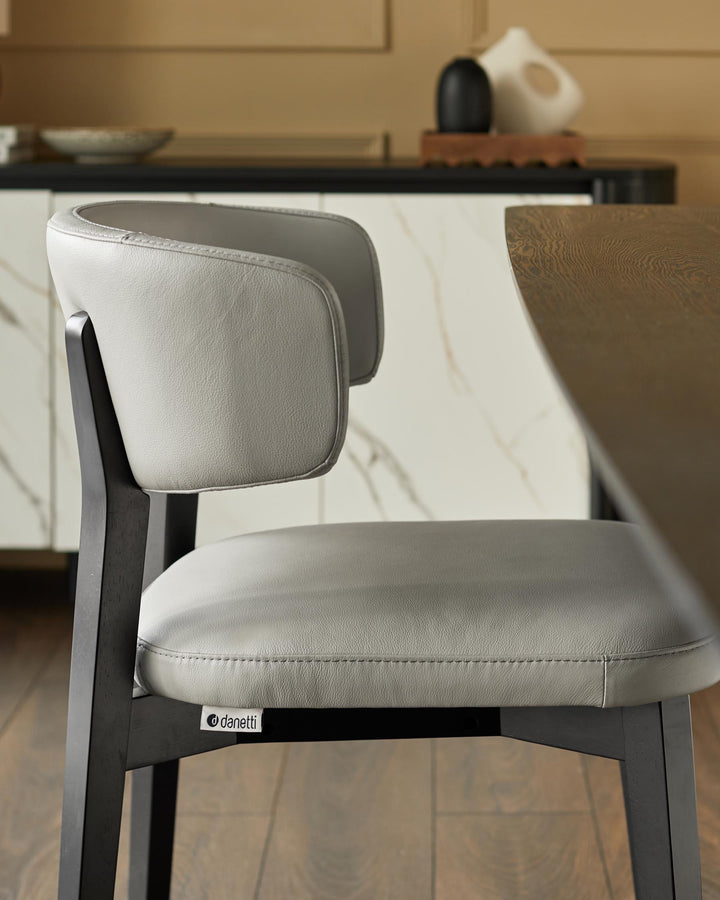 Close-up of a grey leather chair with dark wood frame in a modern dining setting.