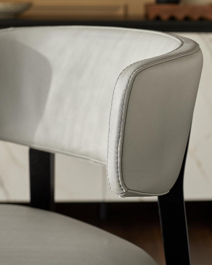 Close-up of a stylish chair with a curved, grey faux leather back and black wooden frame, showcasing modern design.