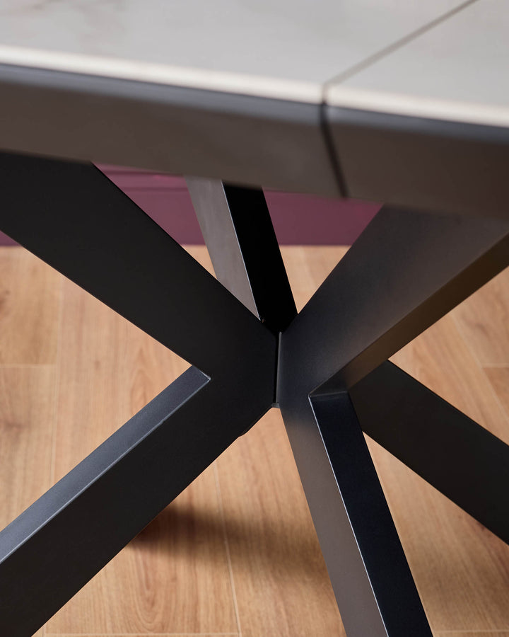 Close-up of a modern dining table featuring a striking black X-shaped base and a light-coloured tabletop.