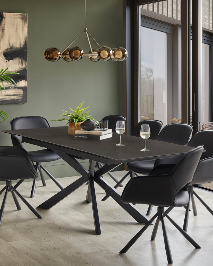 Dining room with a modern table and 8 black chairs, lit by a stylish chandelier. Books and wine glasses are on the table.