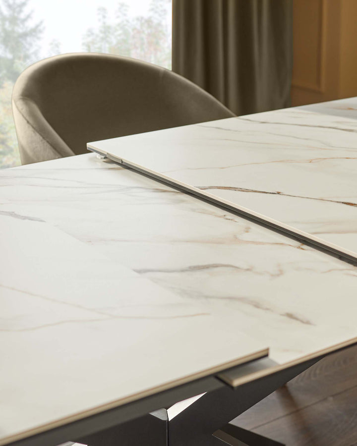 Close-up of an extendable marble dining table with a dark metal frame and upholstered chair in the background.