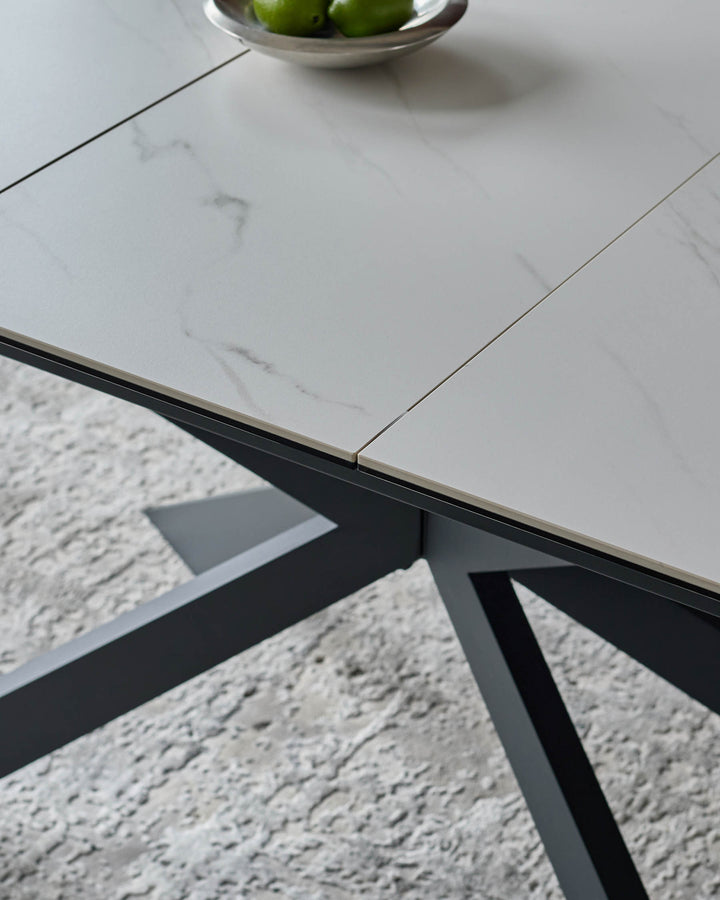Hayden extending dining table in white ceramic with black metal base, angled detail shot showing tabletop and frame.