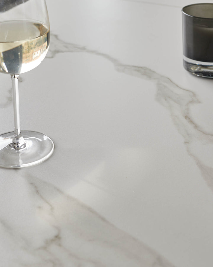 White marble dining table with elegant veining, styled with wine glasses and beverages.