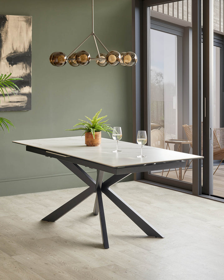 A modern dining table with a white top and dark metal base, set with wine glasses and a fern.