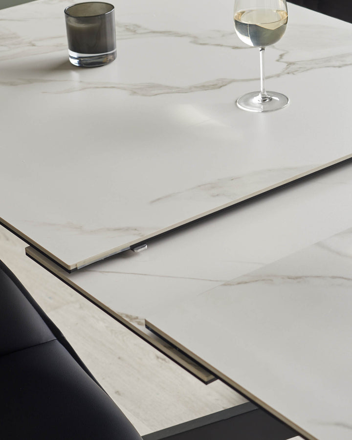 A modern dining table with a white marble effect extending top, set with a wine glass and candle.