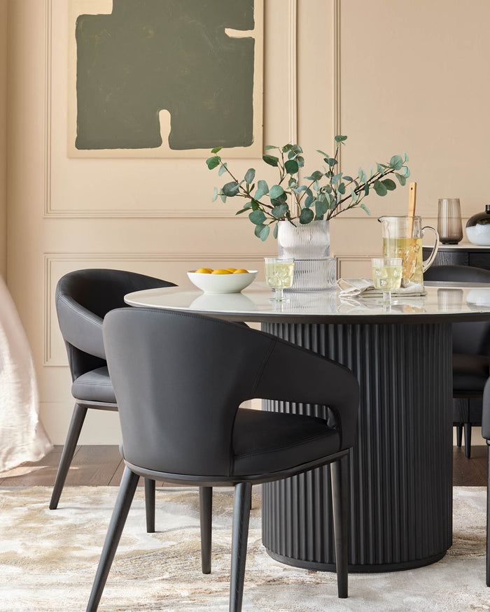 A modern dining set featuring a round marble table with a ribbed base and stylish black leather chairs.