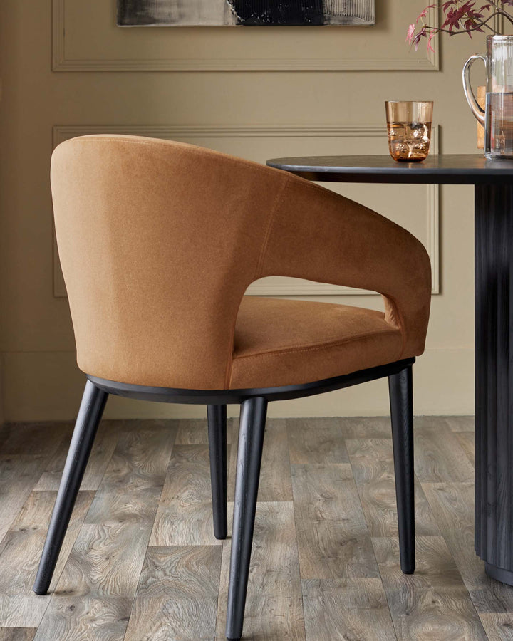 A tan-coloured chair with black legs sits next to a black table. There is a glass and a jug on the table.